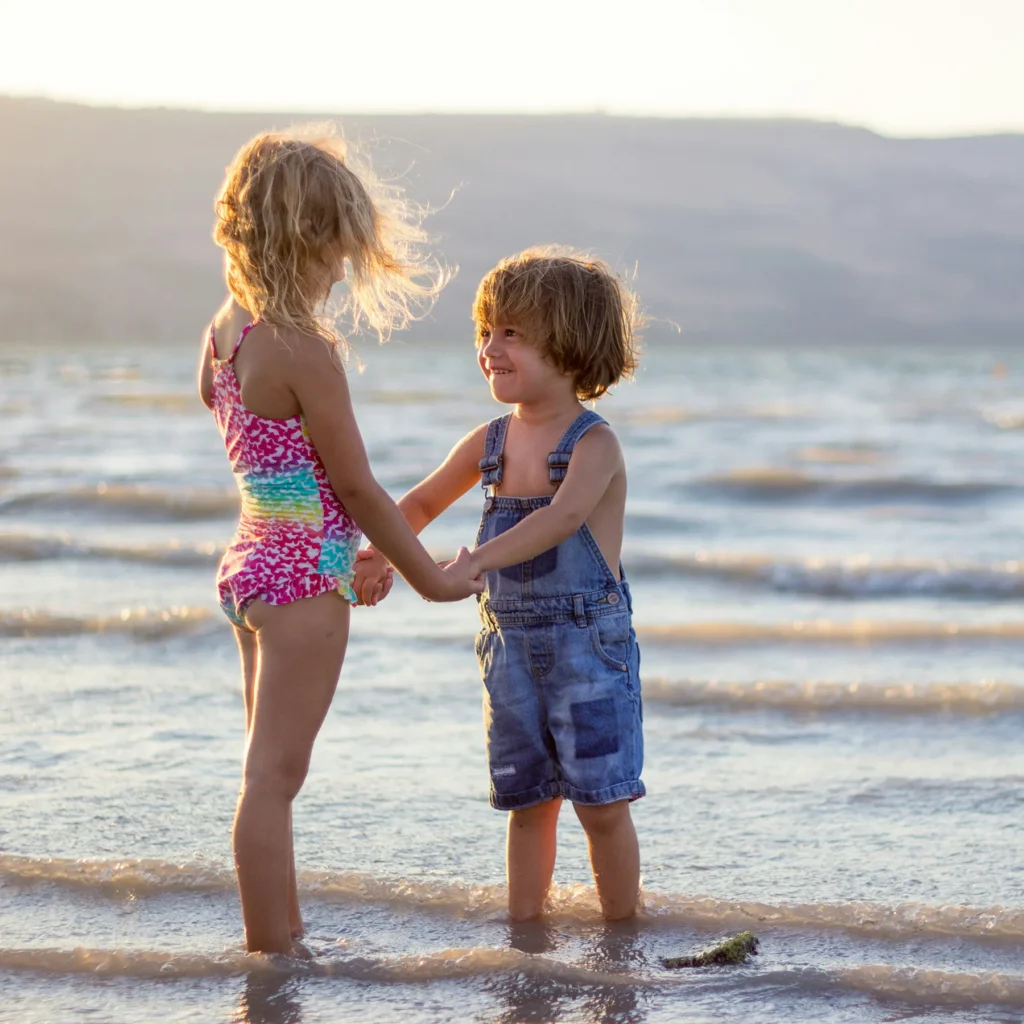 2 kids holding hands on a beach